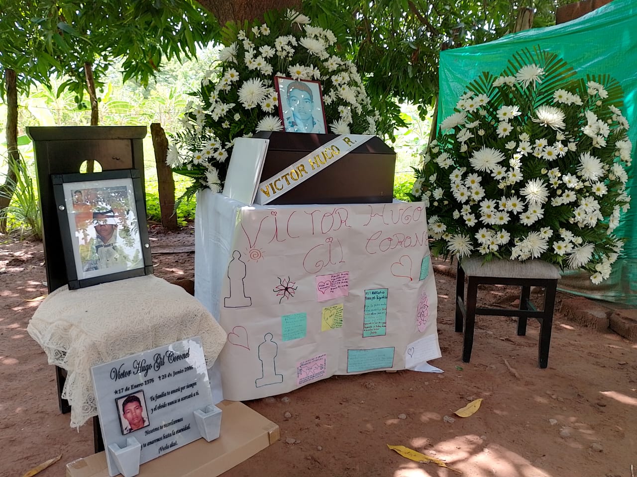 El cuerpo de Víctor en un féretro junto con un arreglo de flores y carteles de su familia