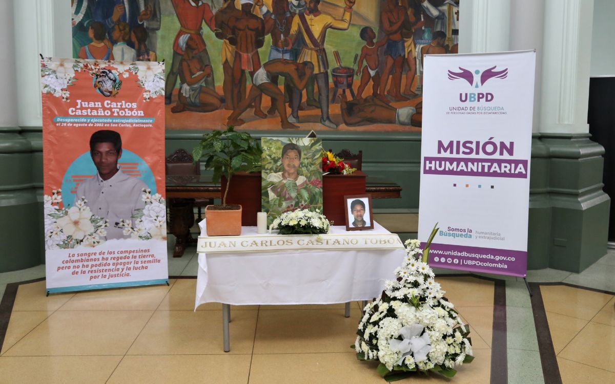 Parada junto al cofre donde reposa su hermano, quien estuvo desaparecido durante 23 años, Martha Isabel no deja de llorar. Cada tanto abre la caja de madera y toca las estructuras óseas que hay en el interior. Sus parientes se acercan y lloran junto a ella. Algunos la abrazan y otros miran la pintura de un cafetal en la que se ve a un muchacho moreno, de nariz achatada y cabello crespo recolectando granos de café. Ese joven es Juan Carlos Castaño Tobón, cuyo cuerpo fue entregado de manera digna por la Unidad de Búsqueda de Personas dadas por Desaparecidas (UBPD).