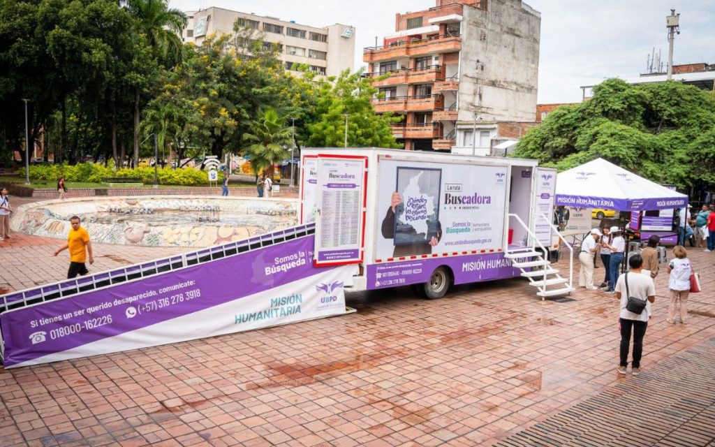 Unidad móvil 'La ruta Buscadora' de la UBPD estacionada en una plaza pública con una rampa de acceso accesible y carpa informativa.