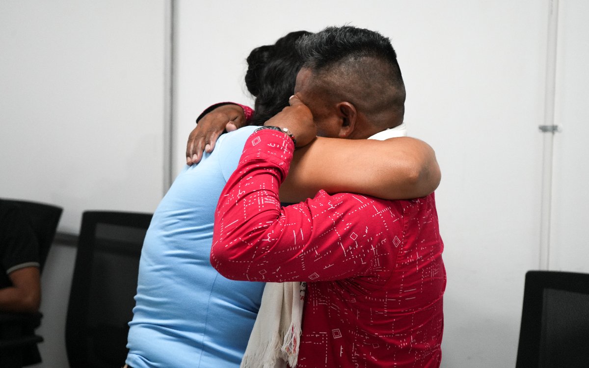 Un hombre con camisa roja estampada abraza fuertemente a una mujer vestida con camiseta azul, conmovido hasta las lágrimas durante un reencuentro.