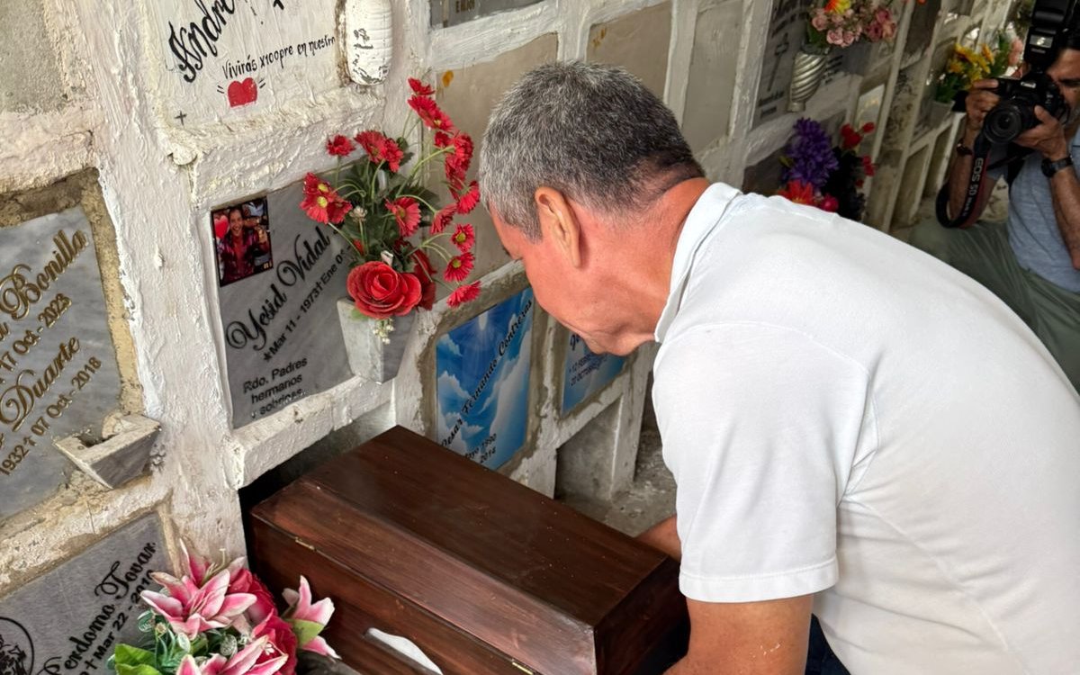 Un hombre inclinado ubica un pequeño cofre funerario de madera en una bóveda de cementerio.