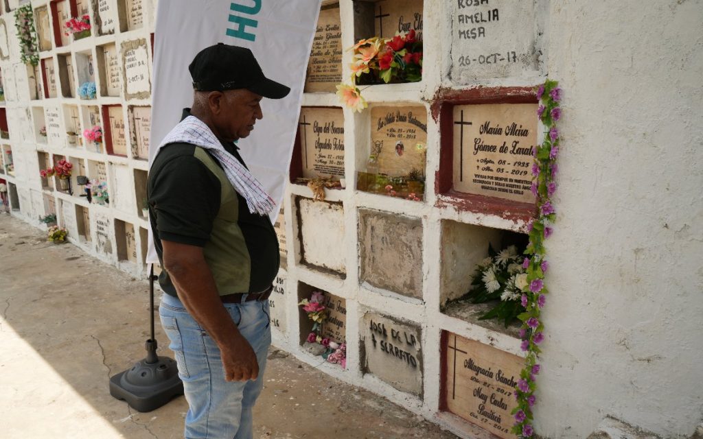 Hombre con gorra negra y toalla al hombro mirando en silencio hacia la bóveda recién sellada en el cementerio.