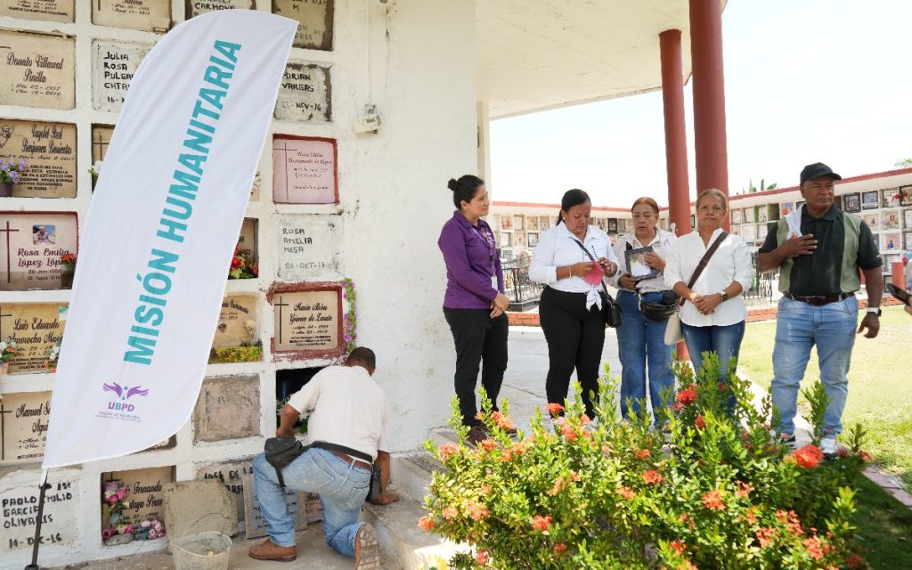 Familiares observan a un operario sellar la bóveda en el cementerio junto a una bandera institucional de la UBPD.