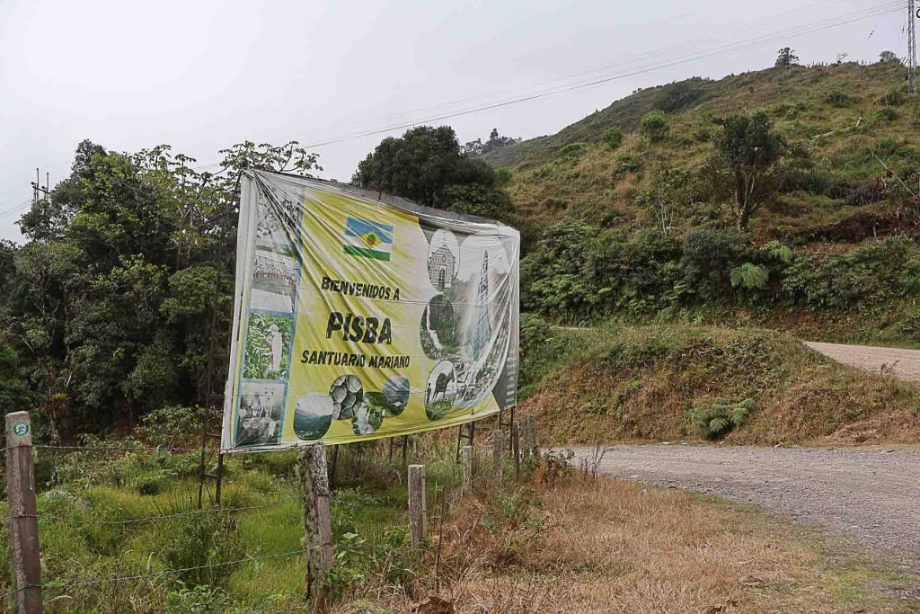 Gran letrero informativo ubicado al borde de una carretera destapada en medio de las montañas de Boyacá, con la bandera de Pisba, imágenes de sitios de interés y el texto "Bienvenidos a Pisba".