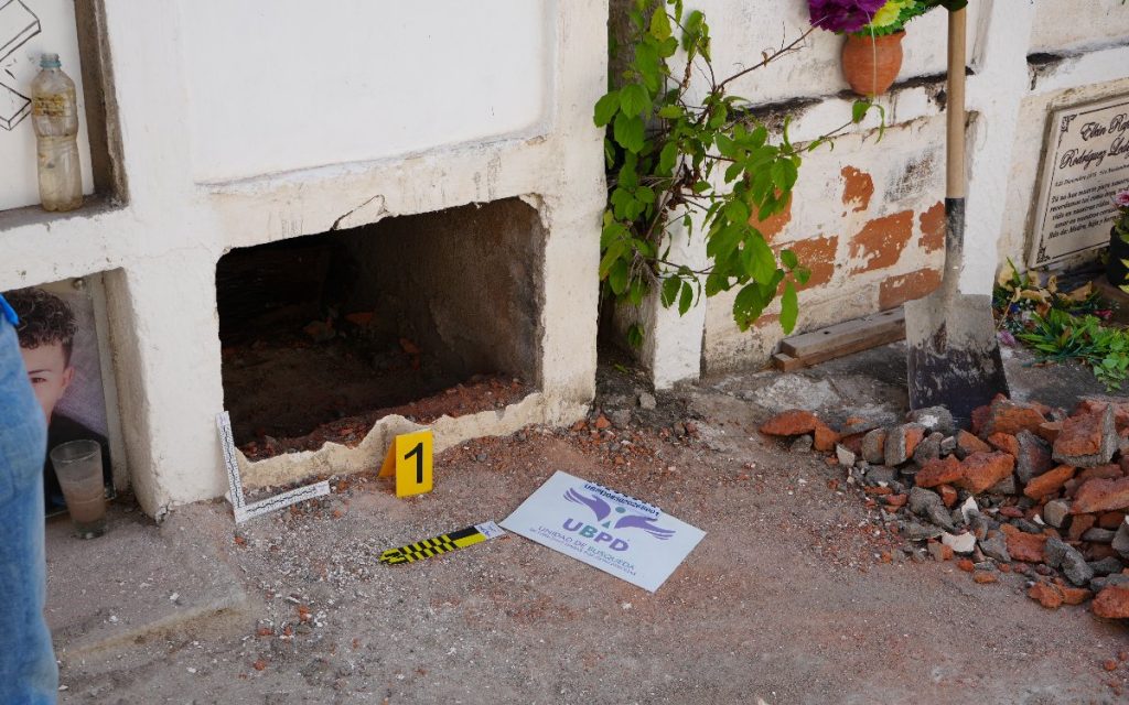 Bóveda cementada abierta en la base, con una pala apoyada al lado, un marcador amarillo con el número 1 y un cartel en el suelo con el logo de la UBPD.