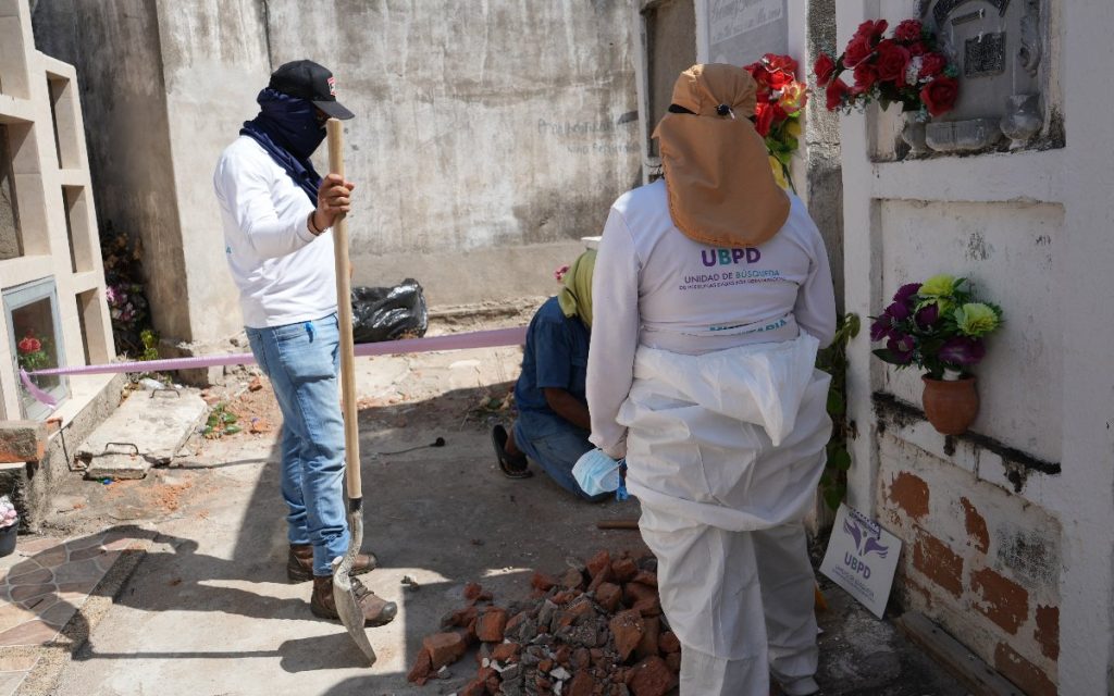 Personal con chaquetas con el logo de la UBPD realizando labores de excavación e inspección junto a una bóveda en un cementerio.