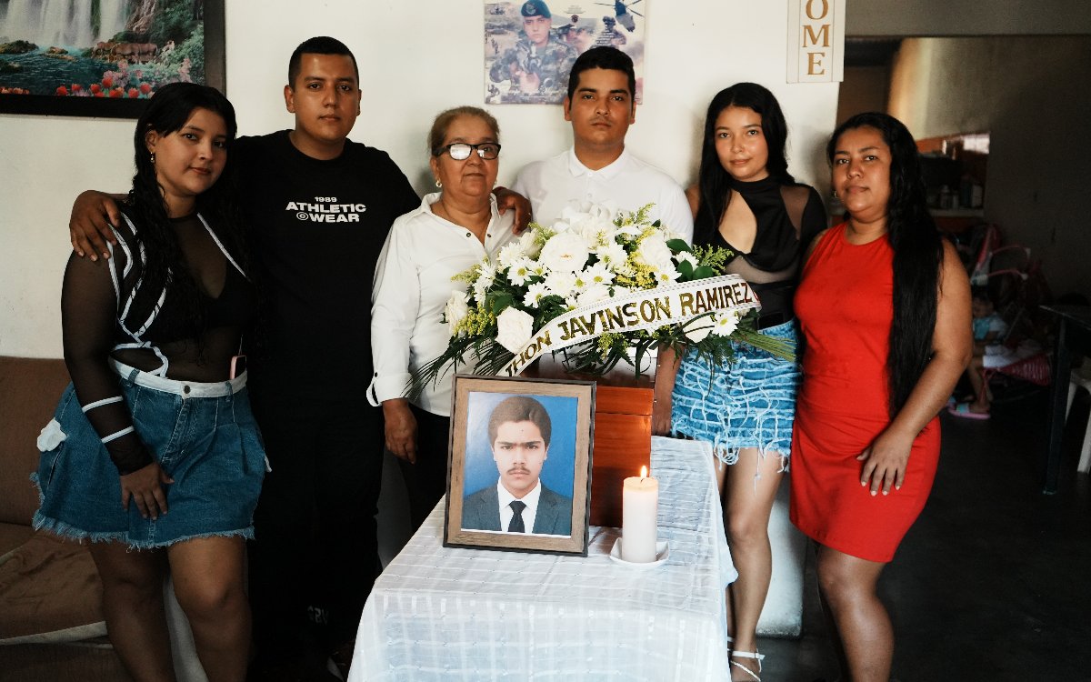Cinco familiares posan con semblante solemne detrás de la mesa que sostiene el retrato, el cofre fúnebre y el arreglo floral de Jhon Jaivinson Ramírez.