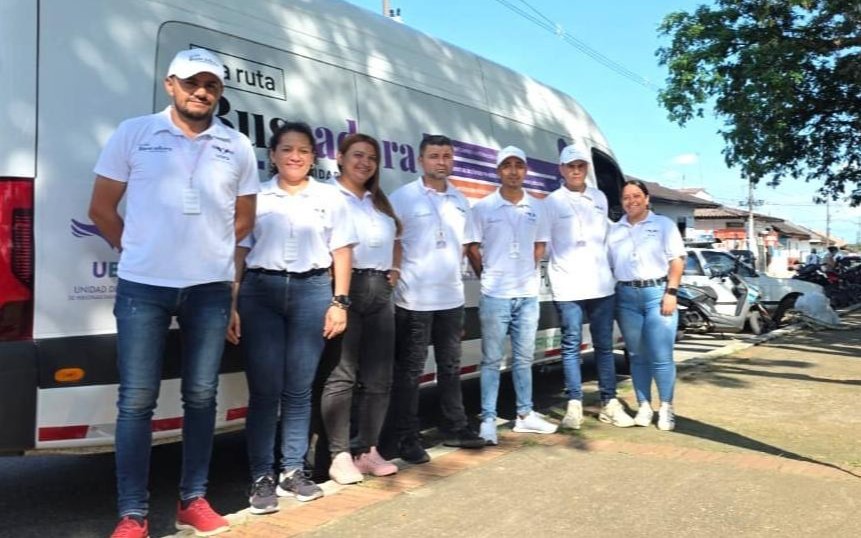 Siete integrantes del equipo de la Unidad de Búsqueda de Personas dadas por Desaparecidas (UBPD) posan alineados frente a un vehículo blanco con la inscripción 