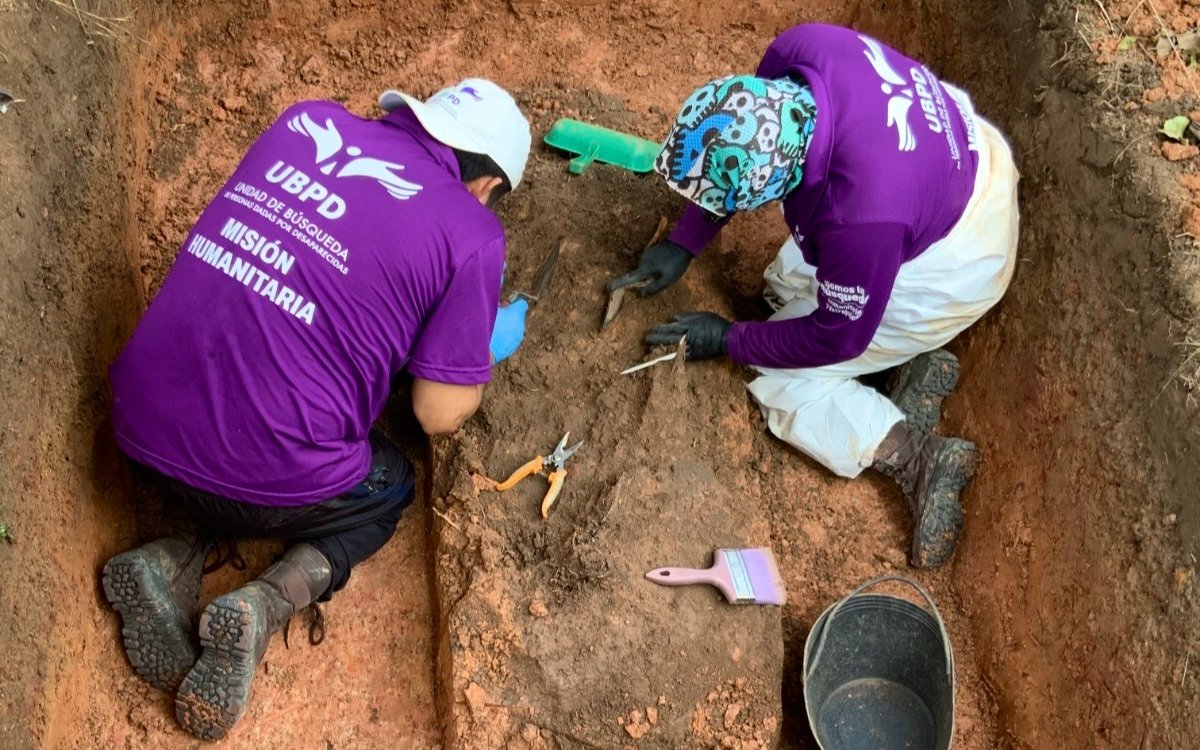 Dos integrantes del equipo técnico forense de la Unidad de Búsqueda de Personas dadas por Desaparecidas (UBPD), vistiendo chalecos morados con la inscripción 