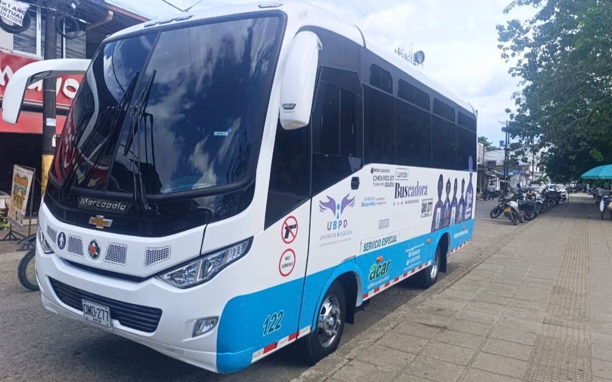 Fotografía en ángulo tres cuartos de un autobús de pasajeros pequeño (microbús) de colores blanco y azul claro. En el lateral del vehículo se observa el logotipo de la UBPD y la gráfica publicitaria con el texto 