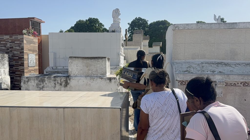 Familiares caminando de espaldas entre los mausoleos y tumbas del cementerio mientras trasladan la urna hacia su lugar de descanso final.